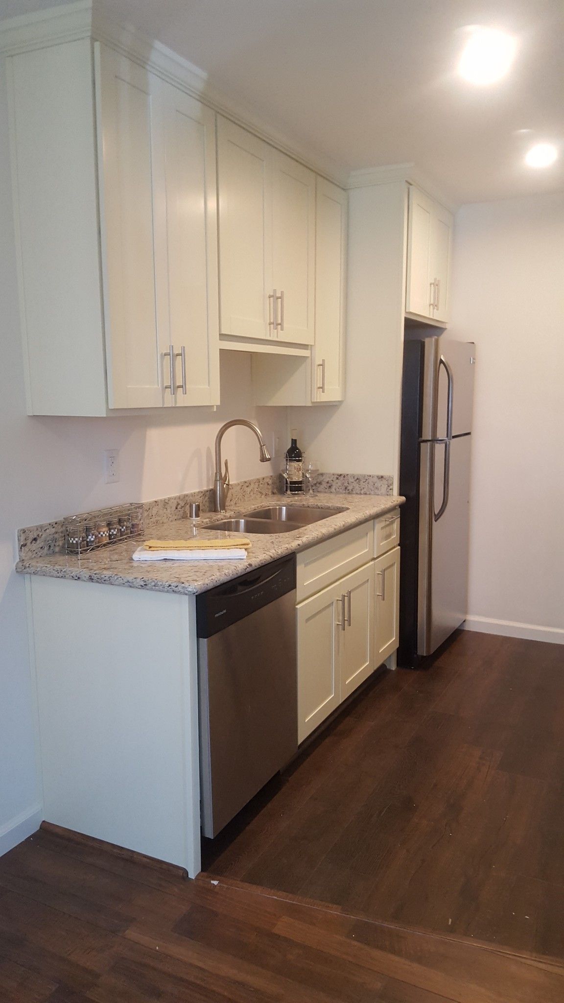 A kitchen with white cabinets , stainless steel appliances , a sink , and a refrigerator.