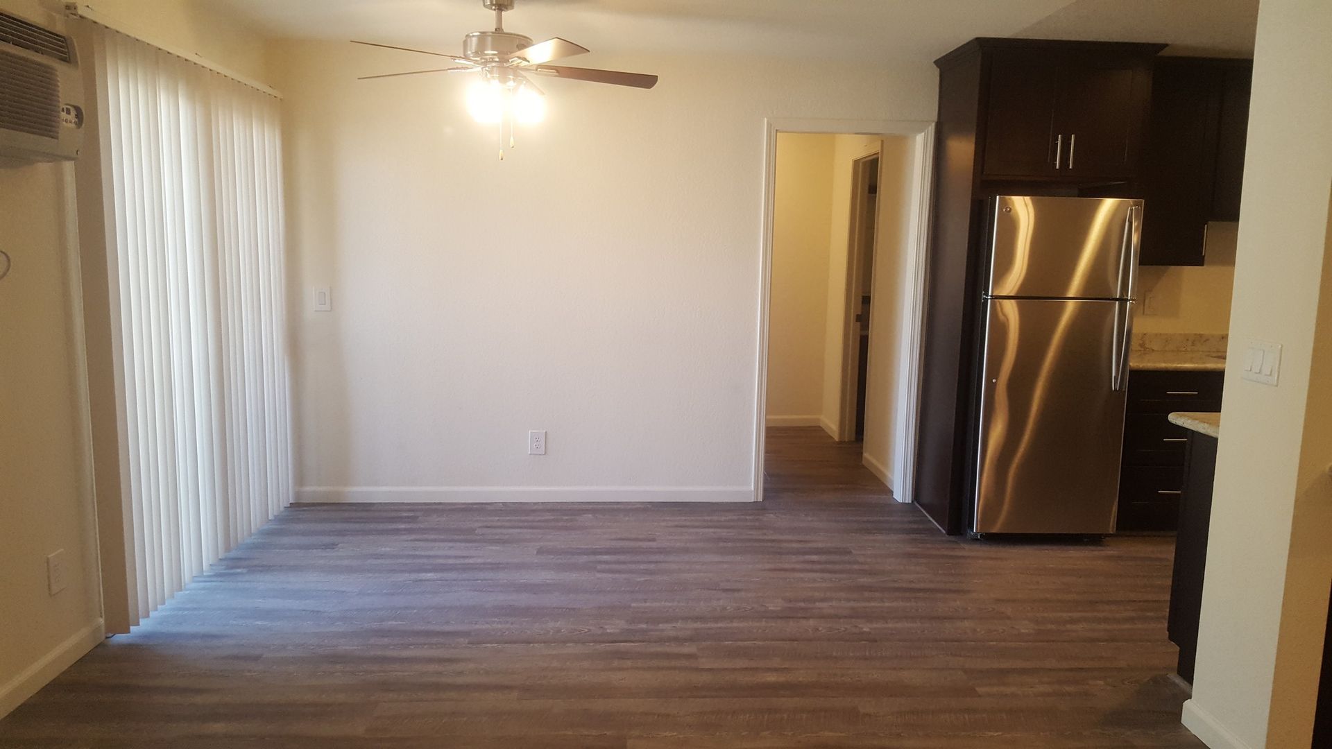 An empty apartment with a stainless steel refrigerator and a ceiling fan.