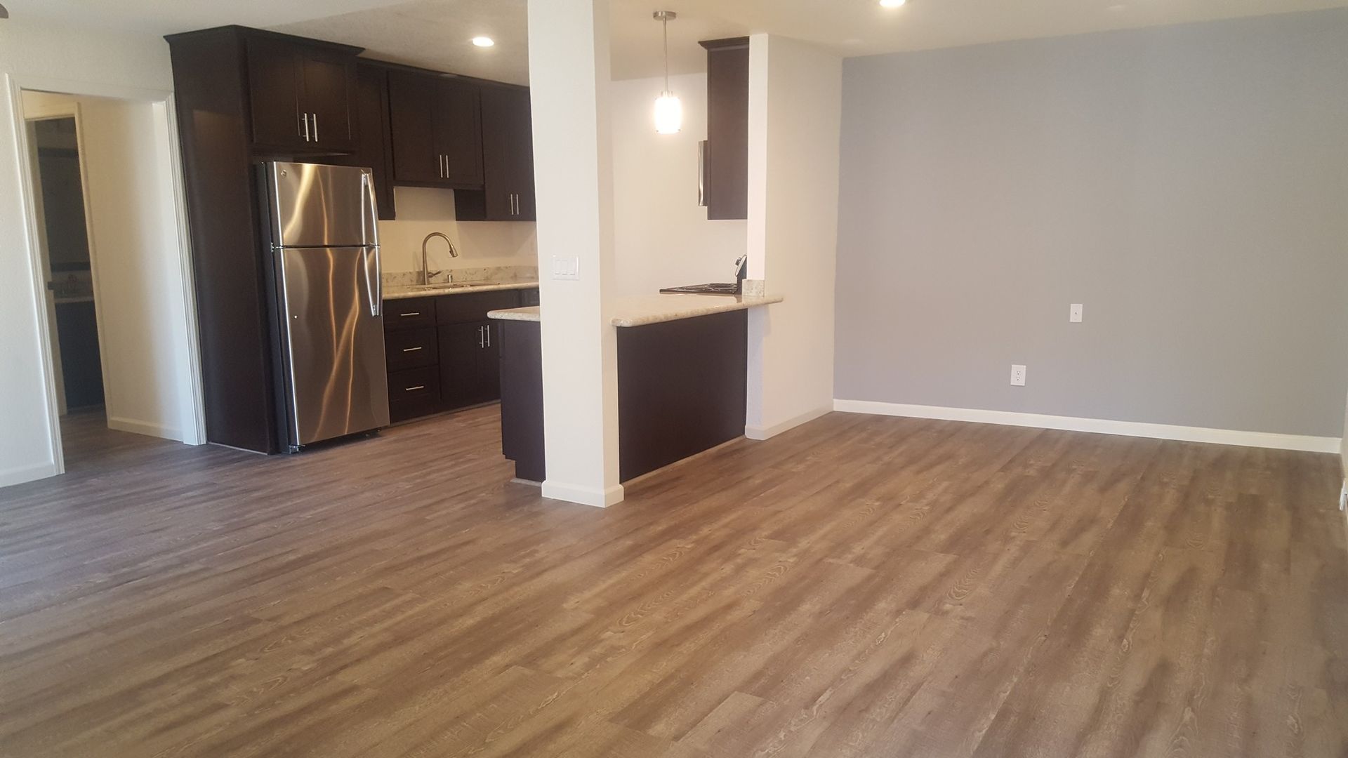 A living room with hardwood floors and a kitchen with stainless steel appliances.