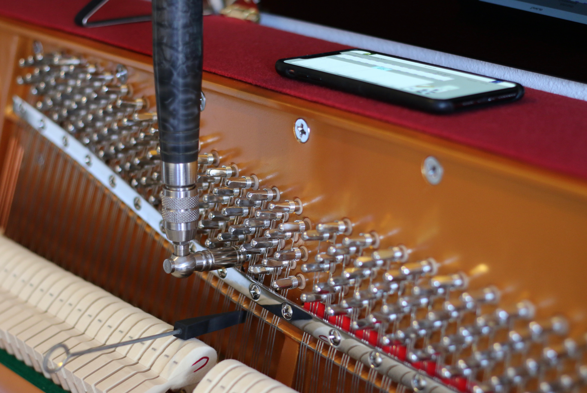Piano tuning in progress, with tuning tool, strings, and phone on the soundboard.