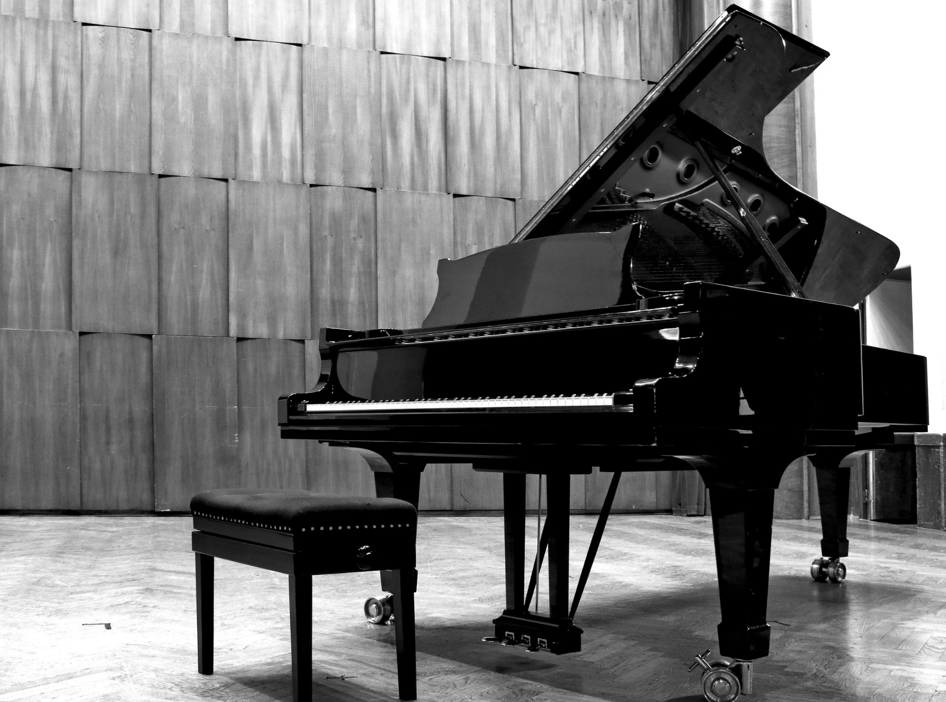 Grand piano with open lid and matching stool in a room with a textured wall.