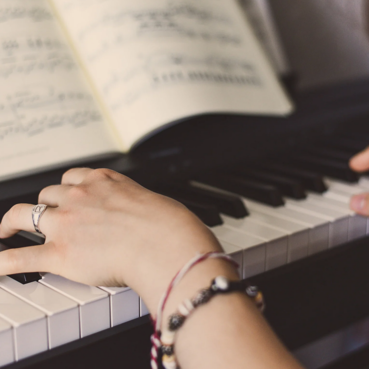 Hands playing piano keys, sheet music visible.