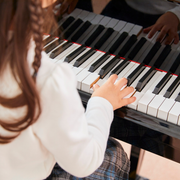 Child playing a piano, hands on the keys. Brown hair, white shirt.