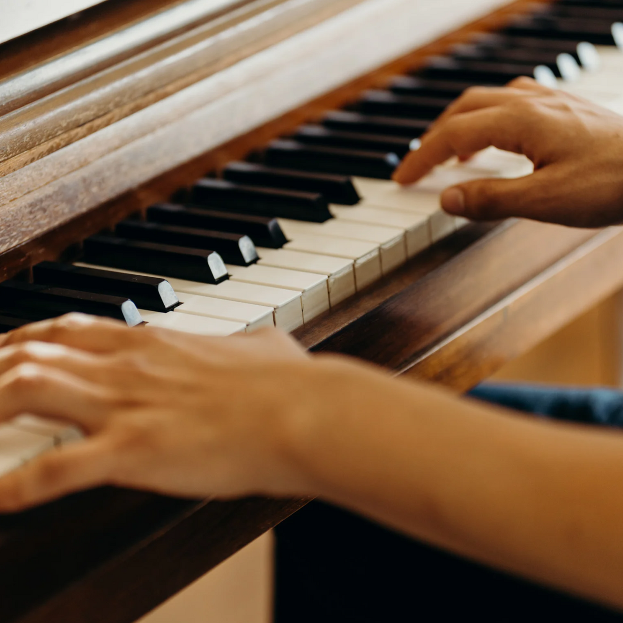 Hands playing a wooden piano; close-up view.