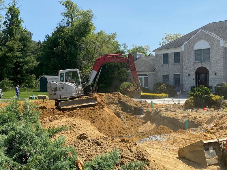 Excavator digging dirt beside a house under construction on a sunny day