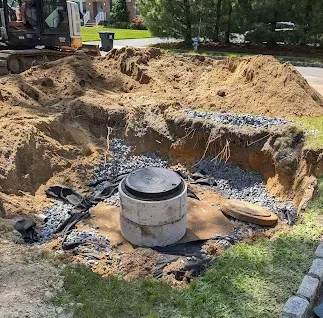 Backyard excavation with a large hole, sand piles, and a concrete septic tank or well structure in the center