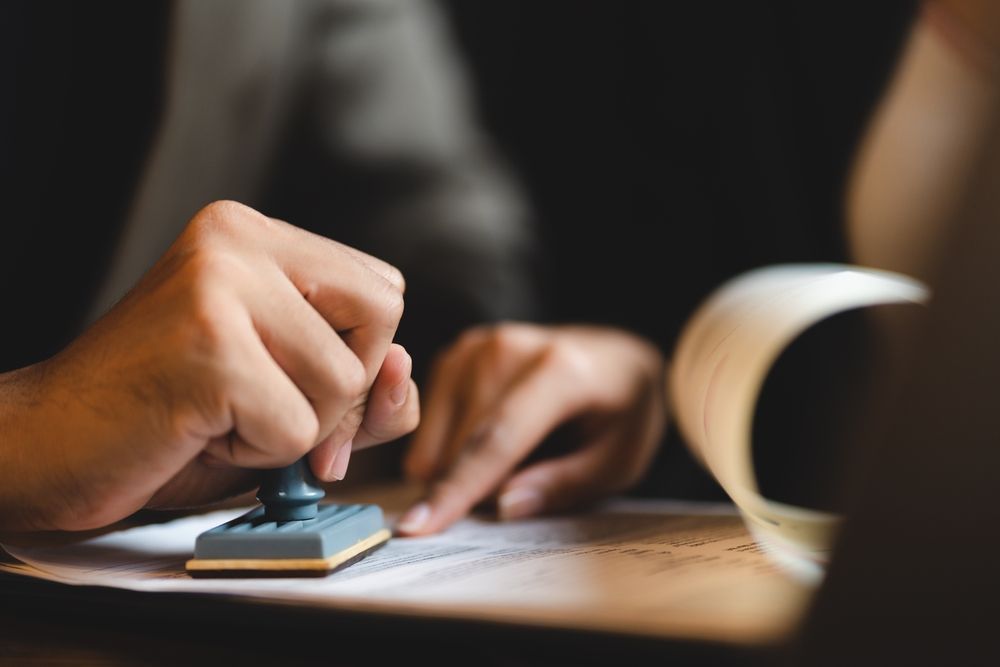 Hand stamping a document on a desk, with a blurred open book in the background