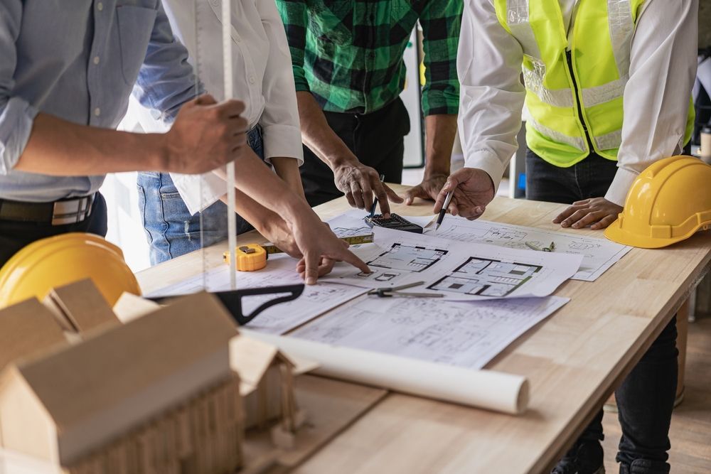 Workers reviewing construction plans at a table, with hard hats and a rolled blueprint in an office setting