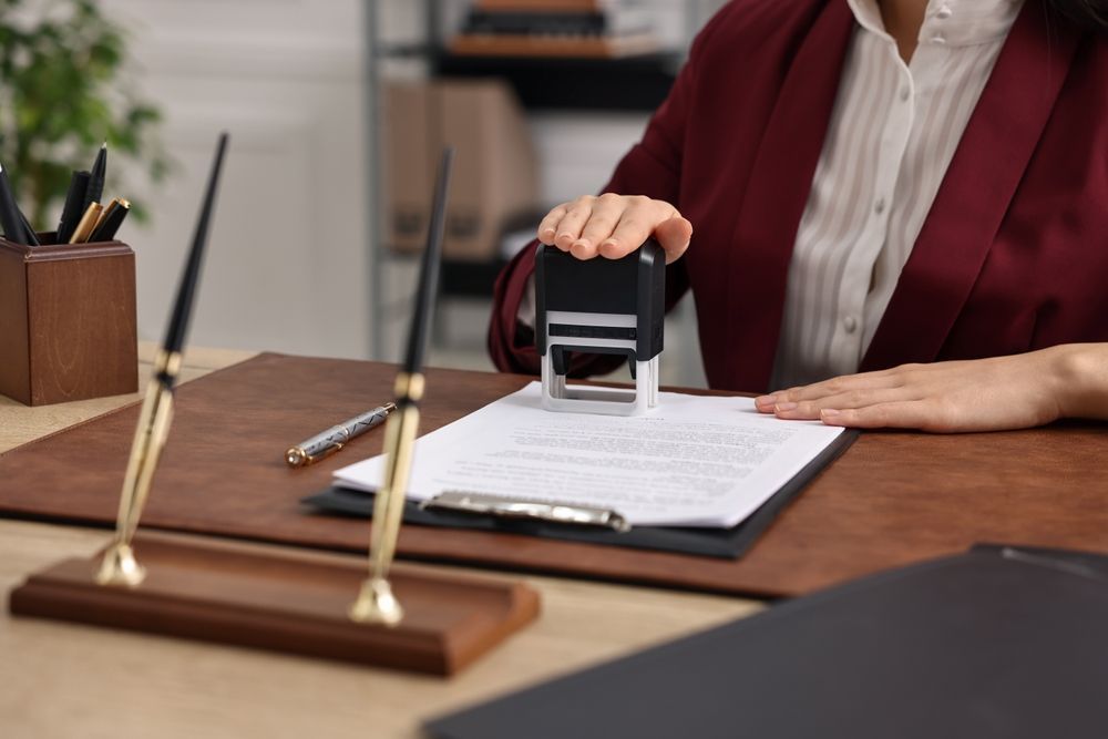 Person stamping a document at a desk with a pen holder and papers in an office setting