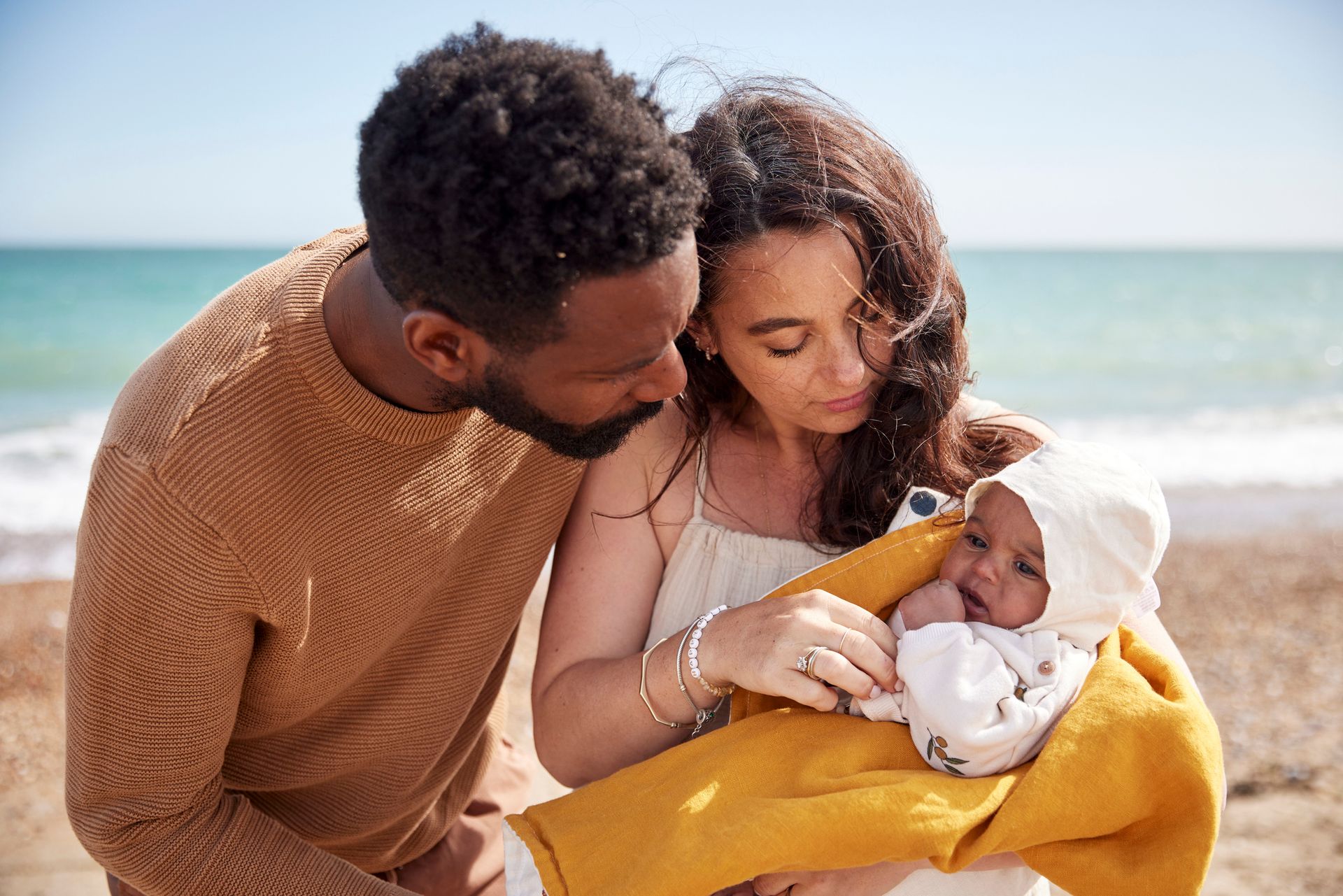 A man and woman are holding a baby on the beach.