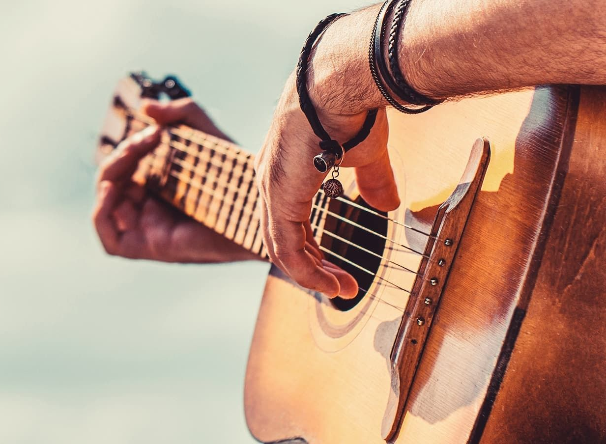 Person's hands playing acoustic guitar with a bright sky in the background.