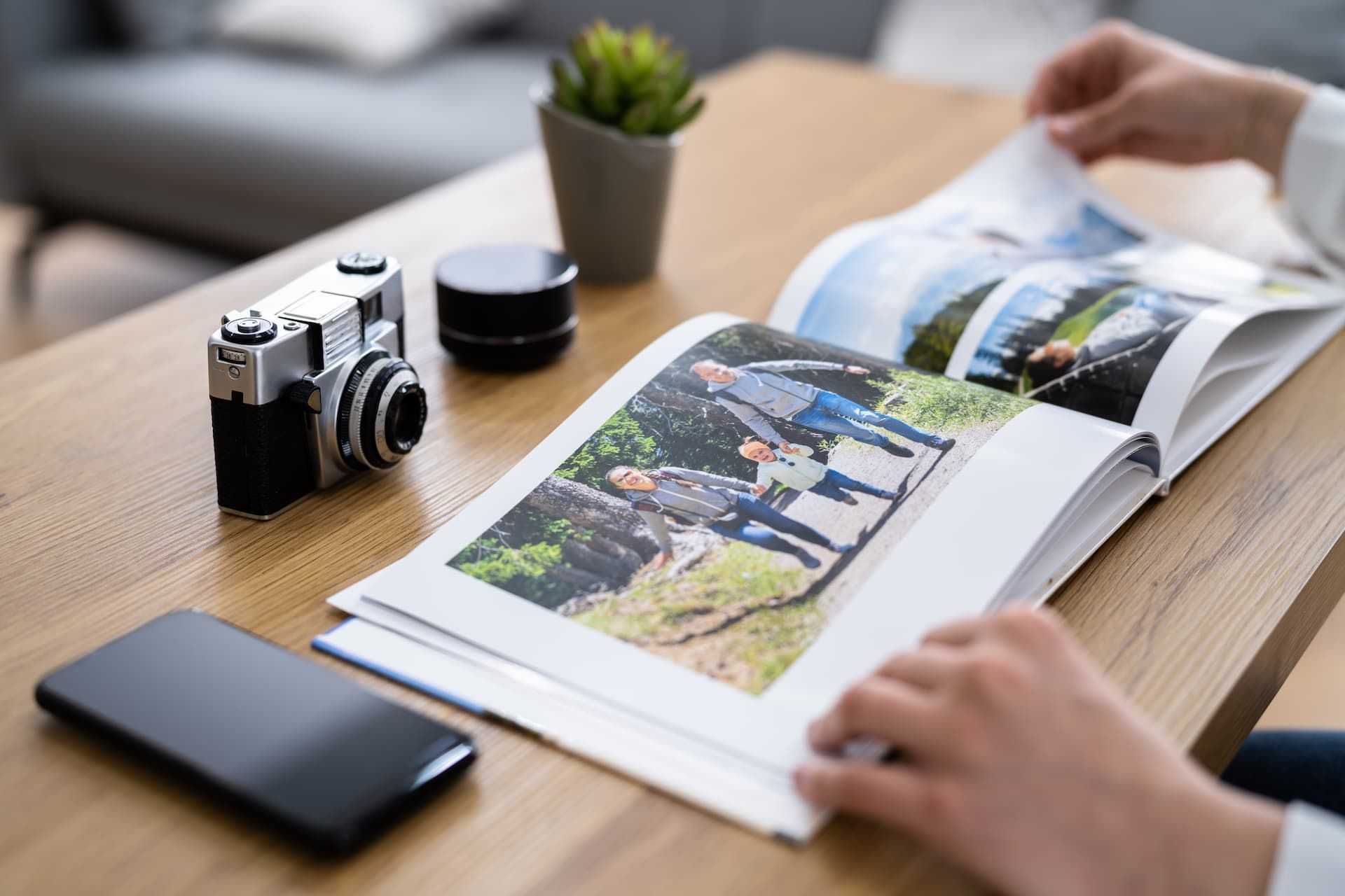 Person flipping through a photo album, with a camera, phone, and plant on the table.