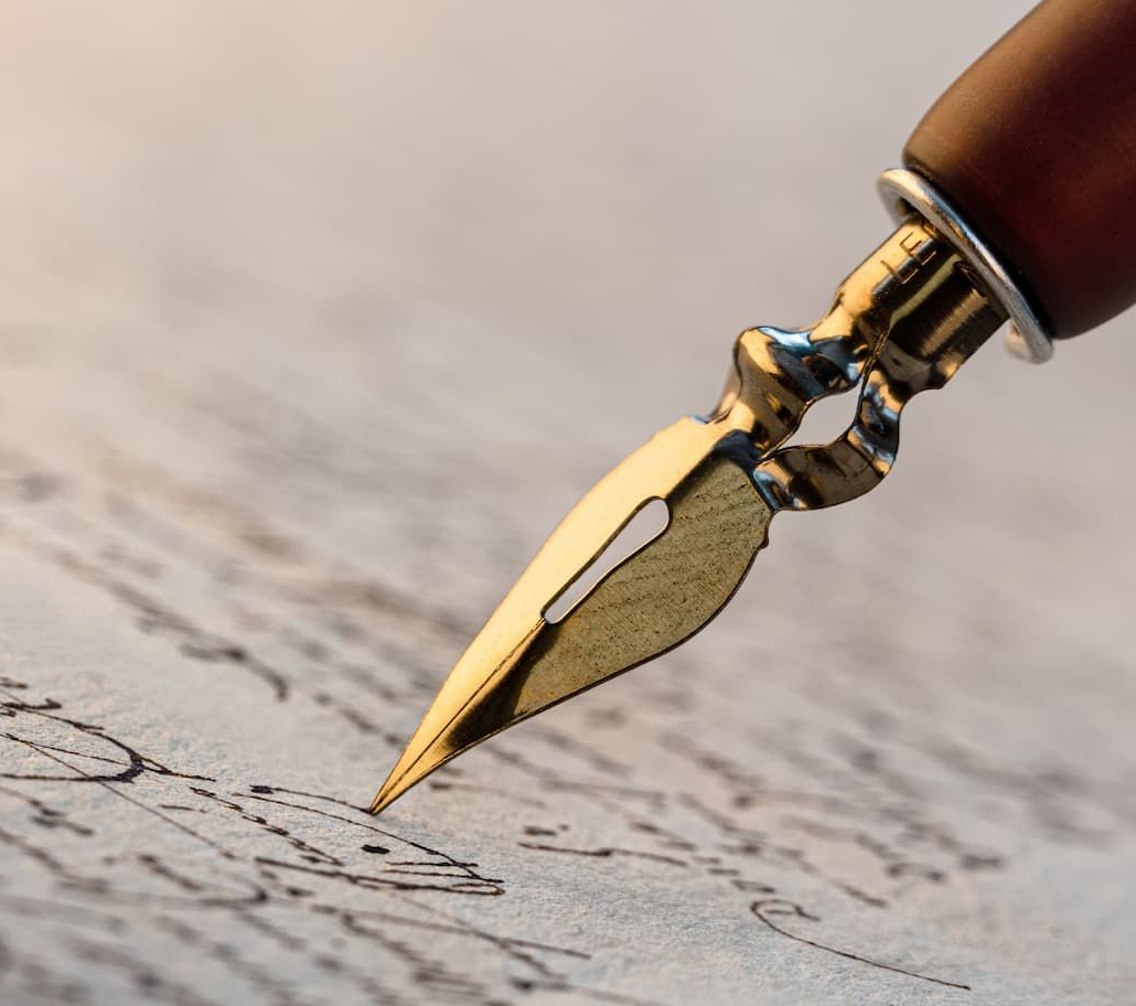Close-up of a gold-tipped fountain pen writing on a textured, blurred paper, likely a letter.