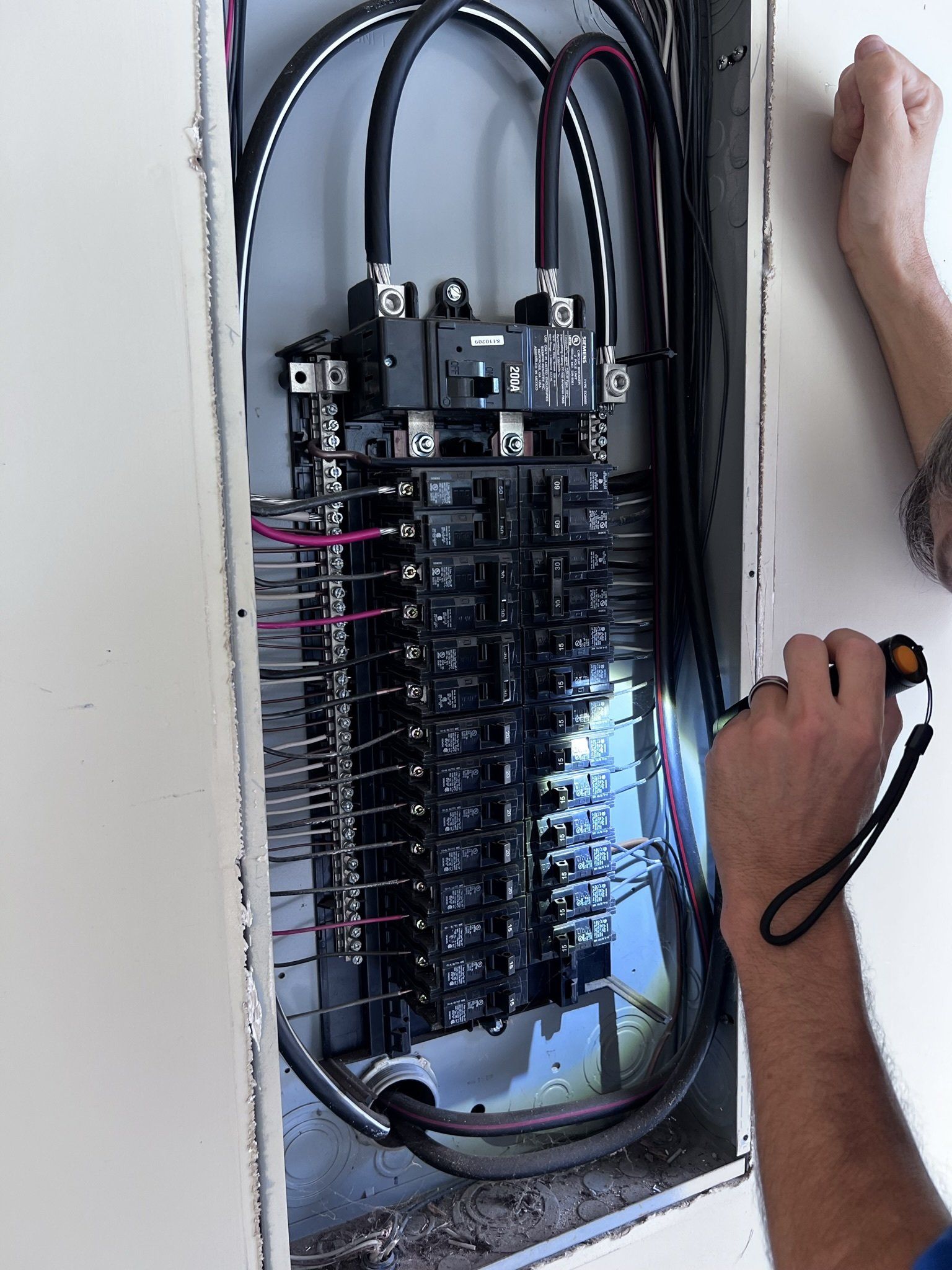 A man is working on an electrical panel with a tape measure