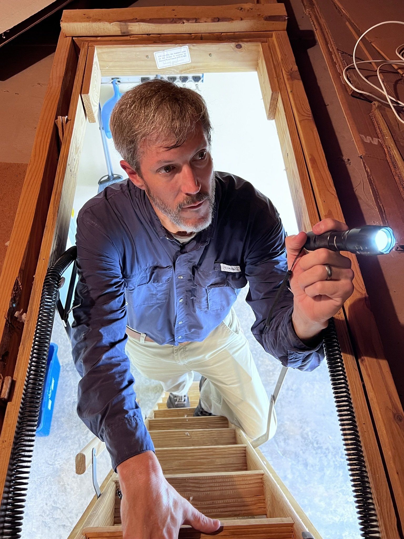 A man is kneeling down on a ladder holding a flashlight.