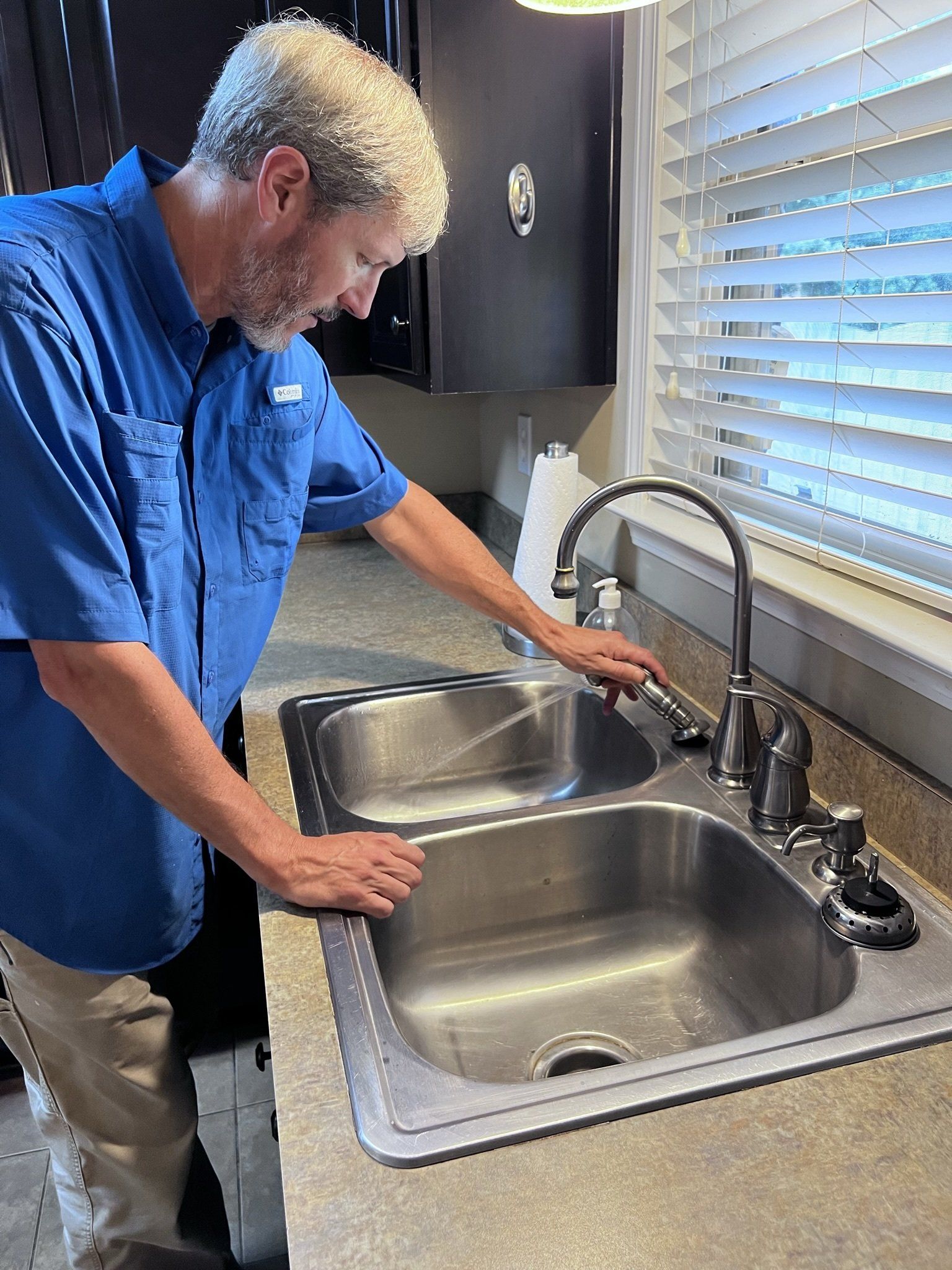 A man in a blue shirt is fixing a kitchen sink.