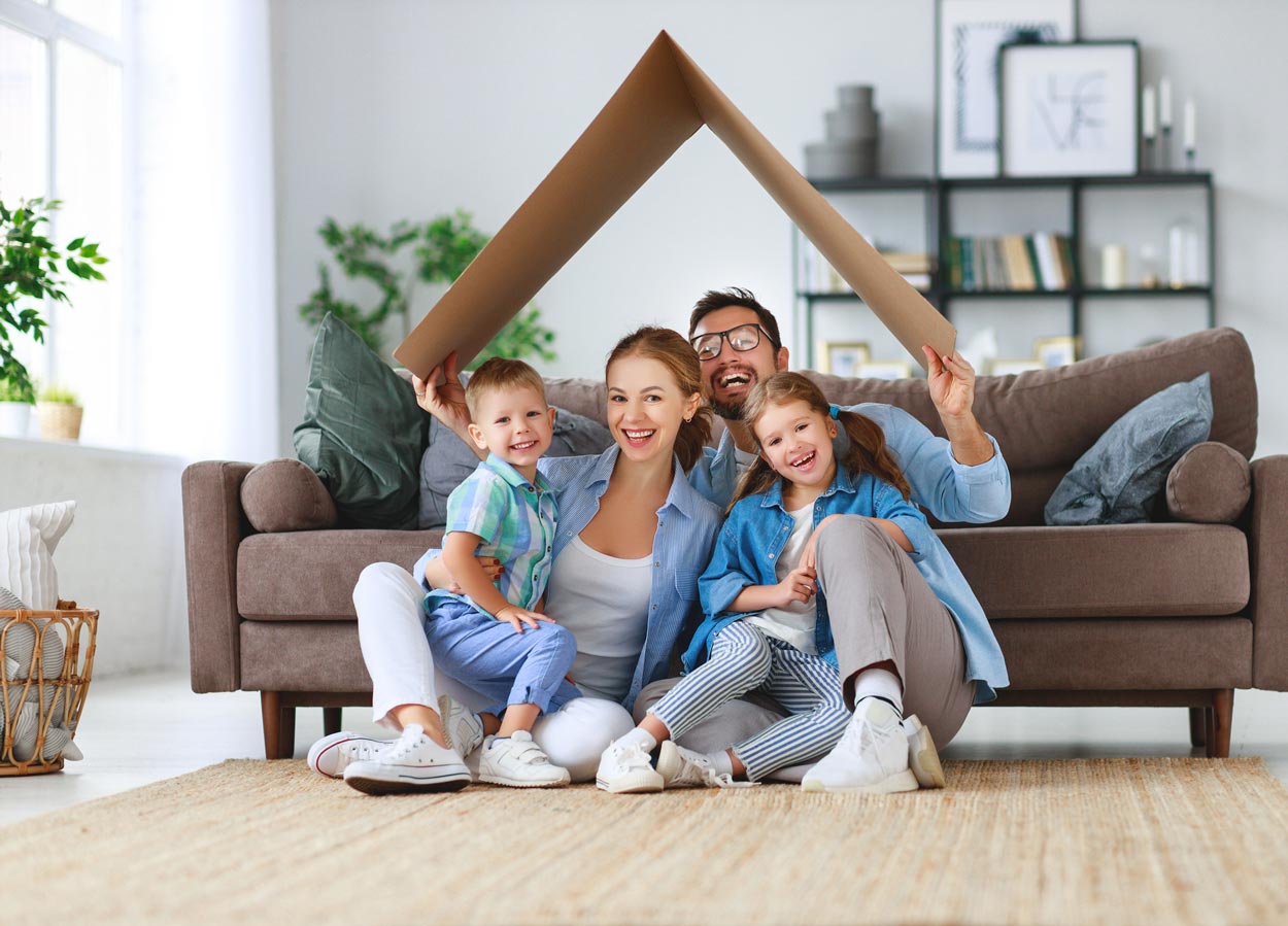 A family is sitting on a couch under a cardboard house.