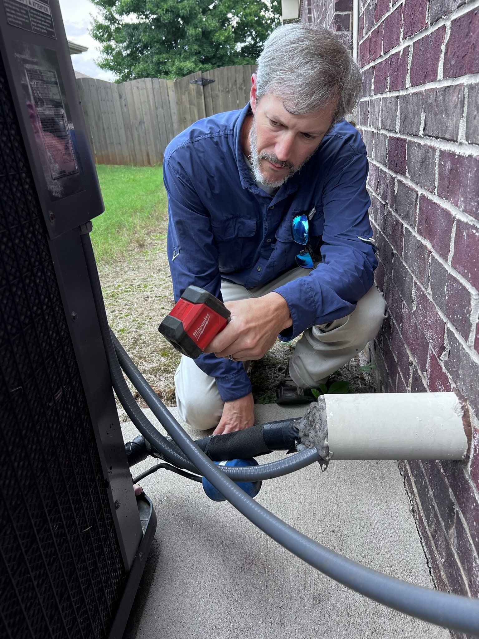 A man is kneeling down next to a brick wall looking at a pipe.