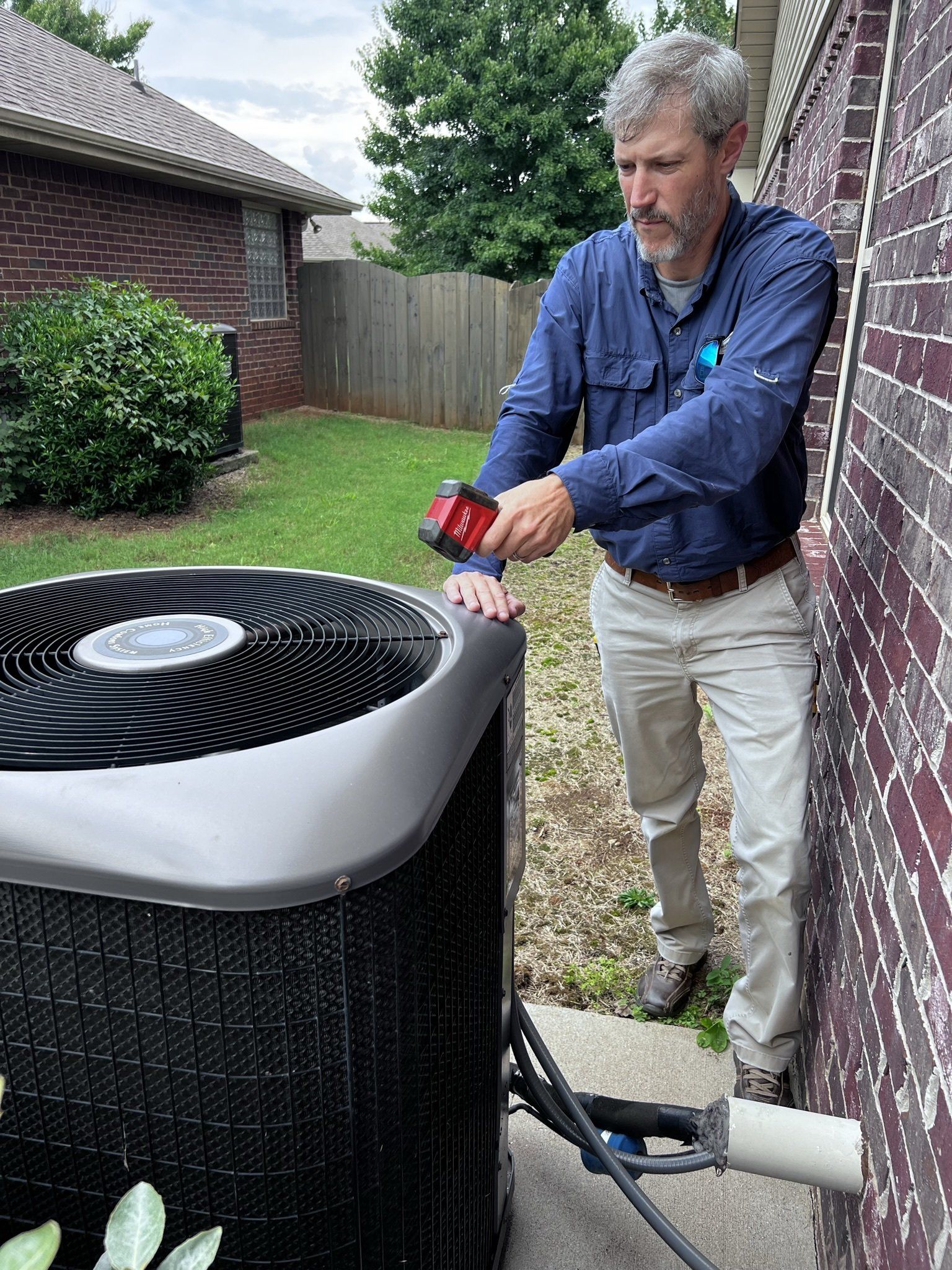 A man is working on an air conditioner outside of a house.