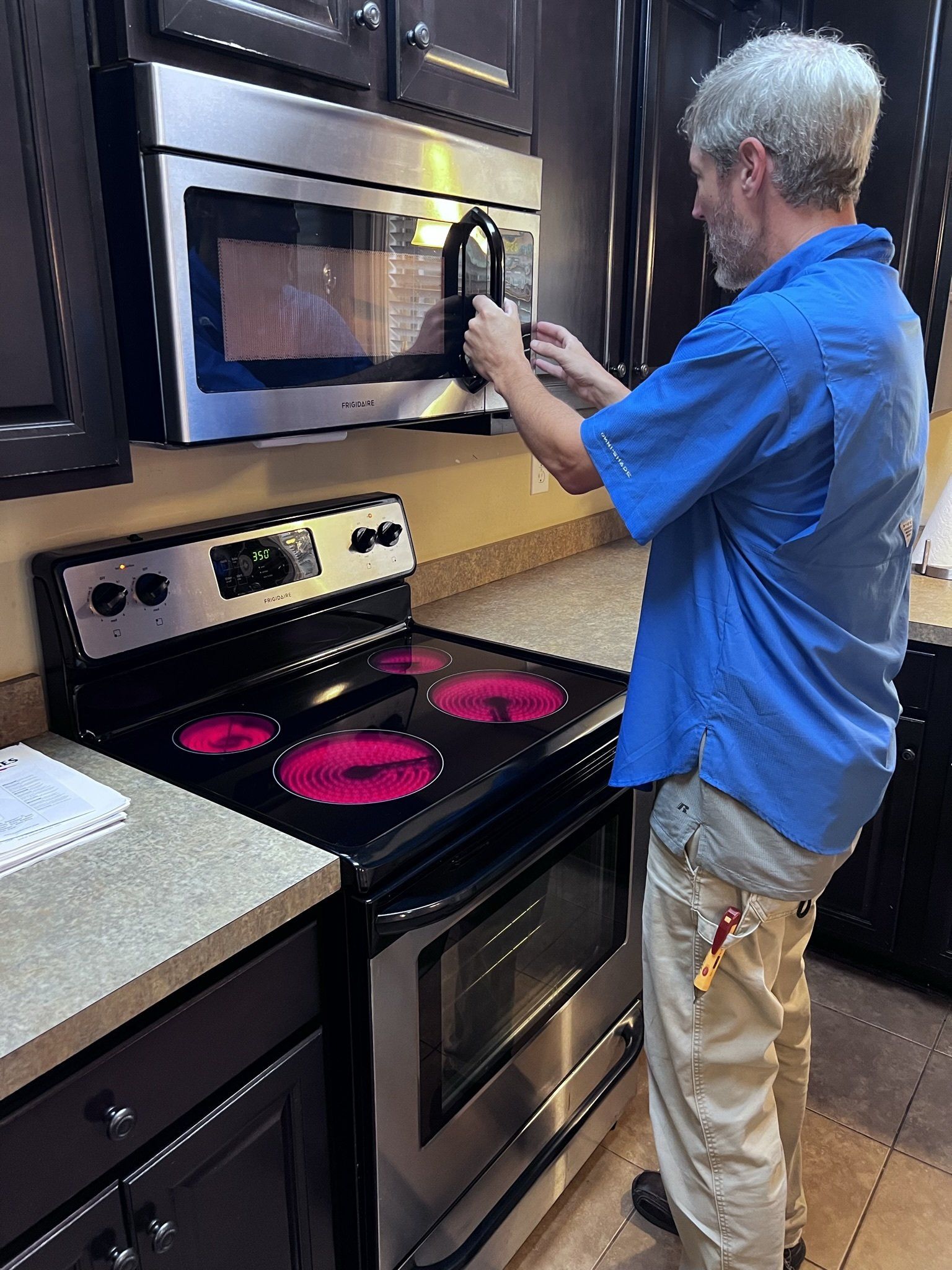 A man is fixing a microwave oven in a kitchen.