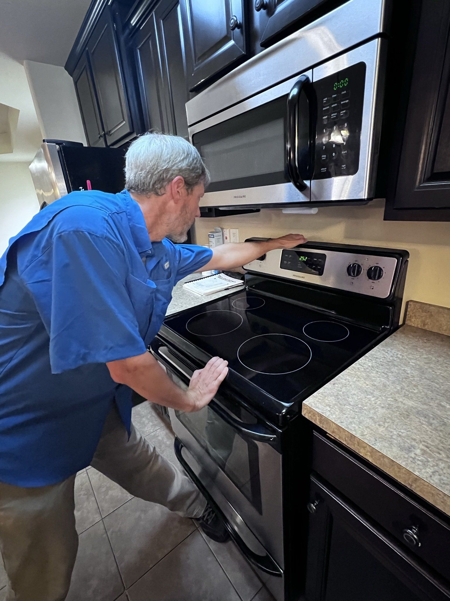 A man in a blue shirt is working on a stove in a kitchen