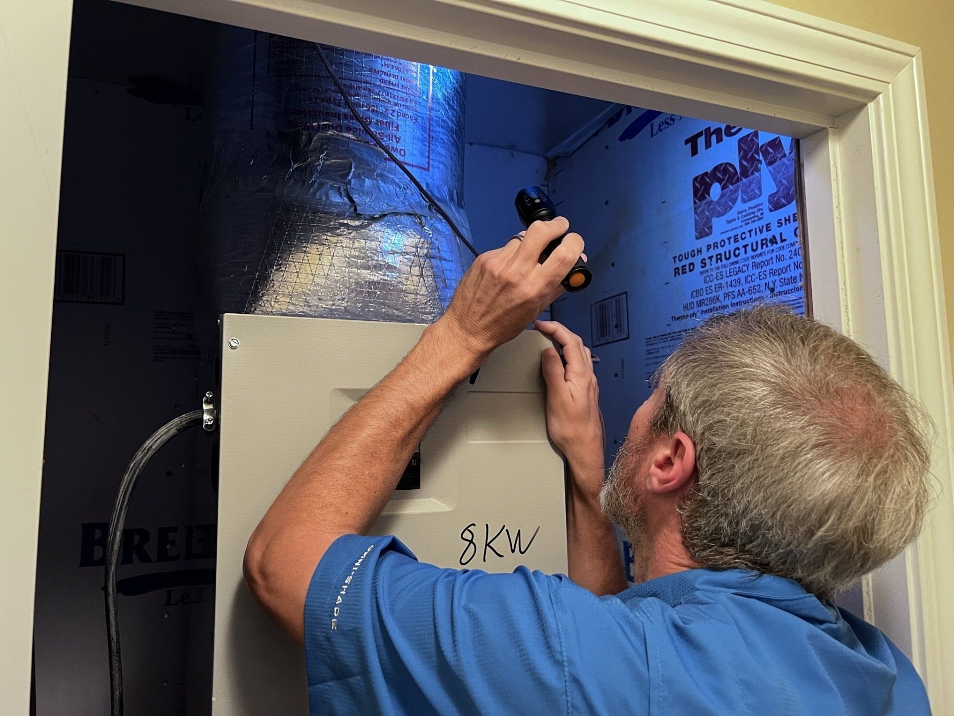 A man in a blue shirt is working on an electrical box.