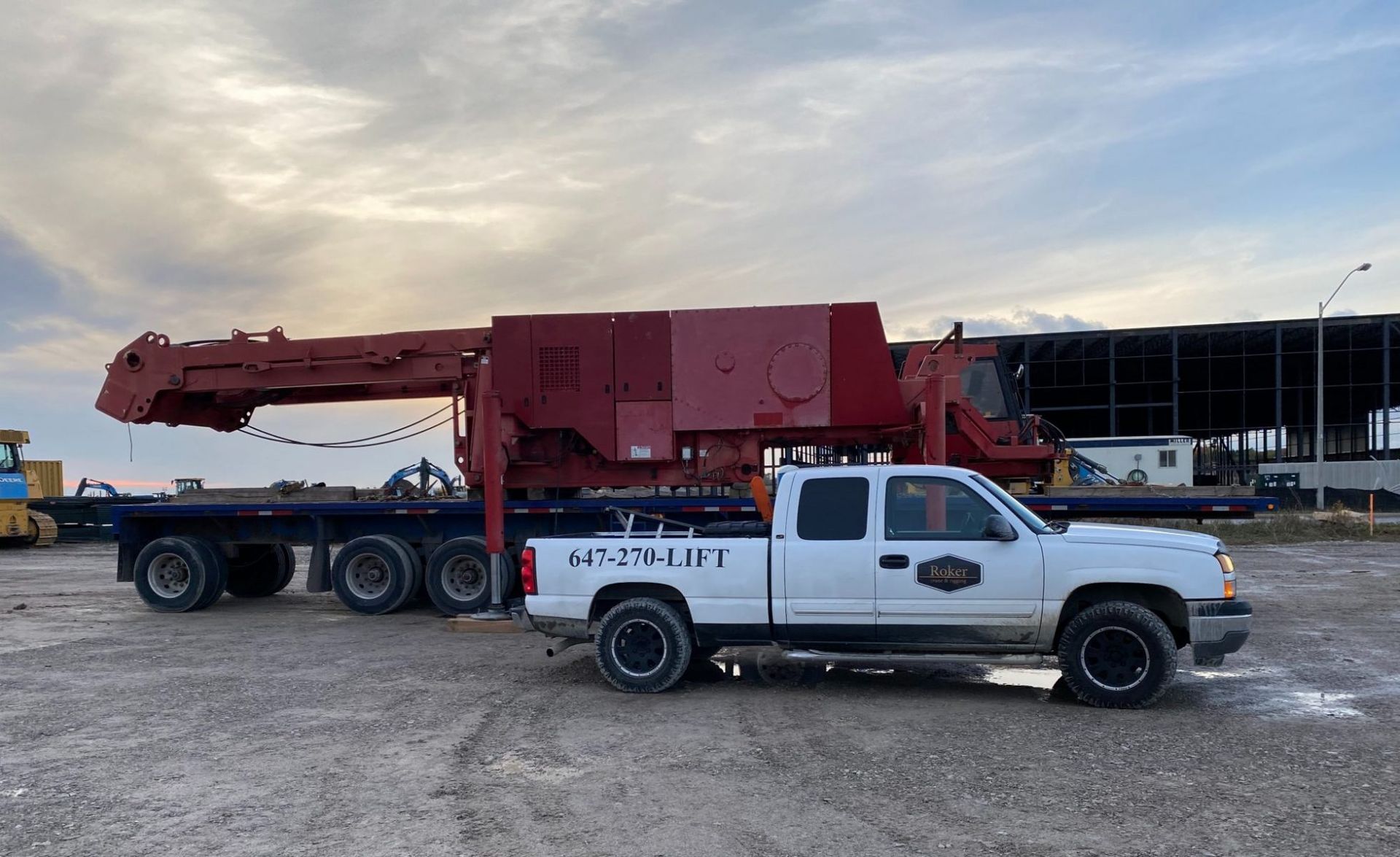 A white truck with a red crane on the back is parked in a gravel lot.
