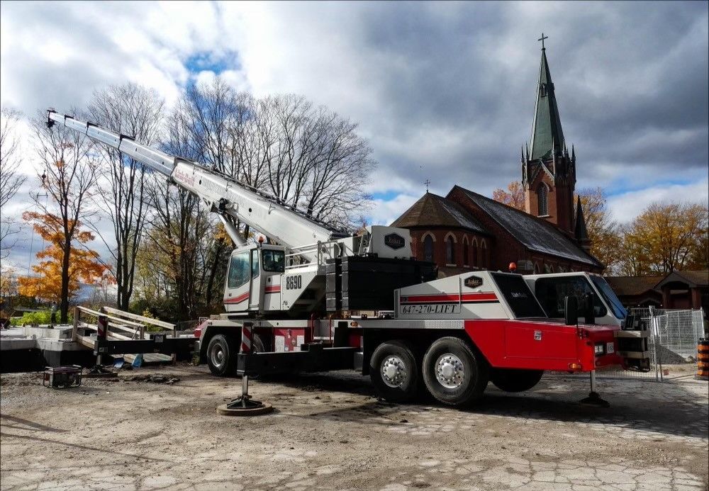 A red and white crane truck is parked in front of a church.