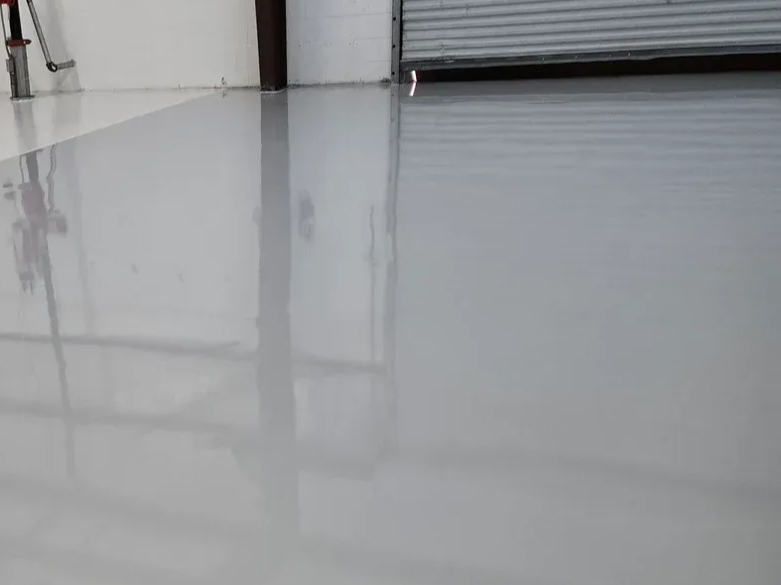 Glossy, light gray epoxy floor reflecting a garage door and wall.