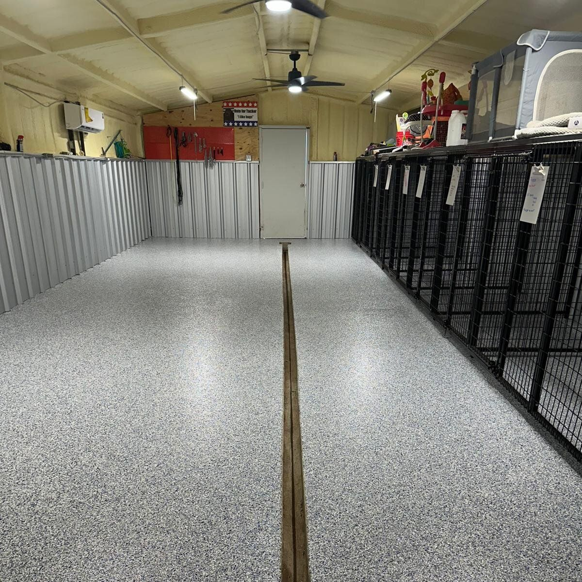 Indoor dog kennel with gray speckled floor, metal cages, and white walls.