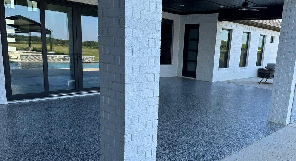 Covered patio with speckled gray floor and white brick columns. Sliding glass doors lead to a pool area.