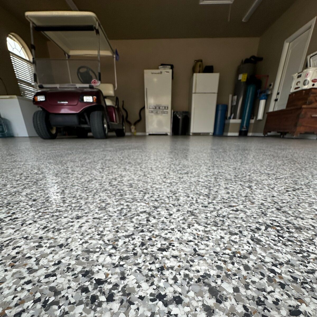 Garage with a speckled epoxy floor, golf cart, refrigerator, and storage.