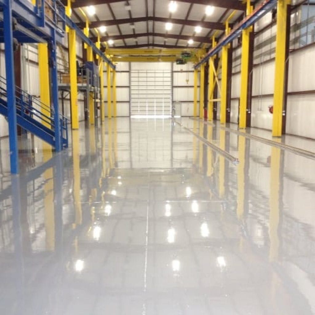 Shiny, light-gray industrial floor reflects overhead lights and metal beams in large warehouse.