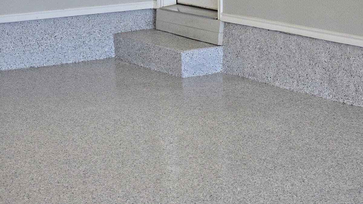 Gray epoxy-coated garage floor and baseboards, with a small step leading to a door.
