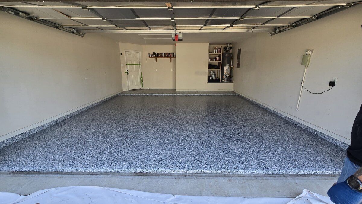 Empty garage with a gray speckled epoxy floor, white walls, and a closed door.