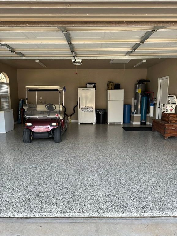 A finished garage with a golf cart, refrigerators, and a speckled gray floor.