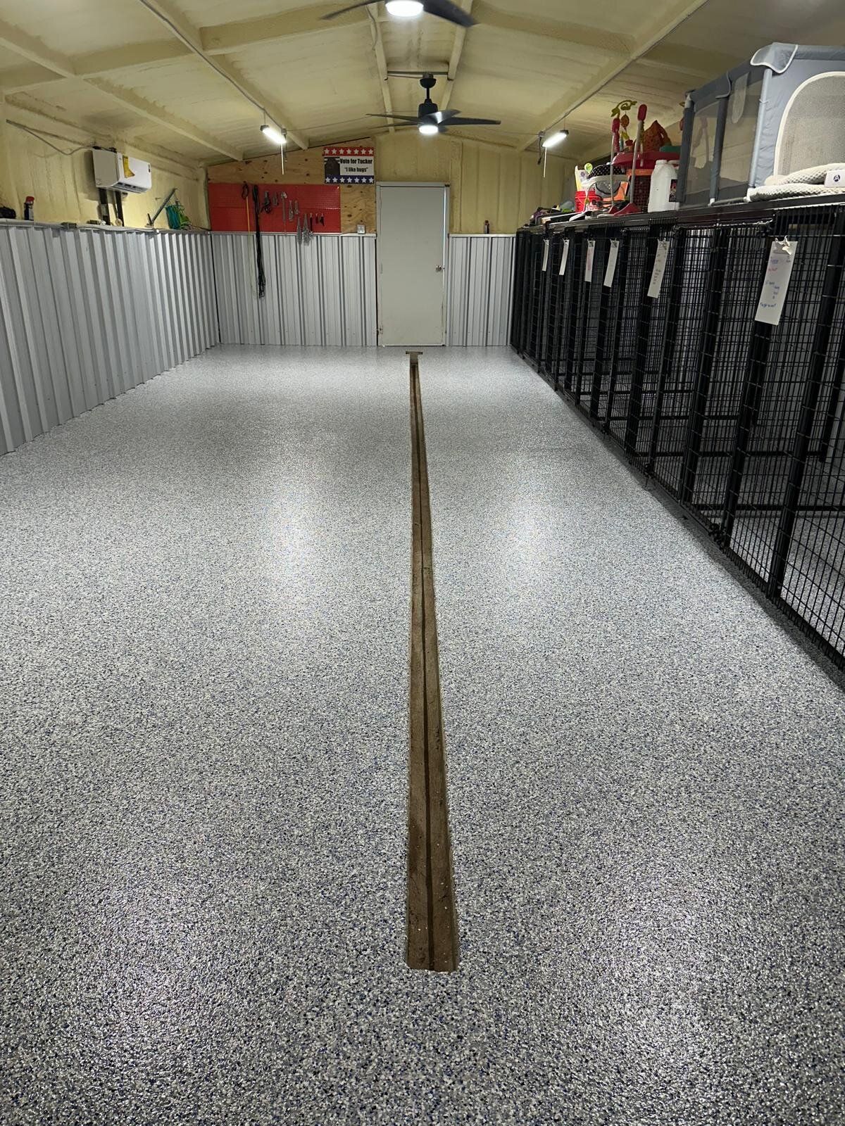 Indoor dog kennel with gray speckled floor, metal cages, and a long wood strip down the center.