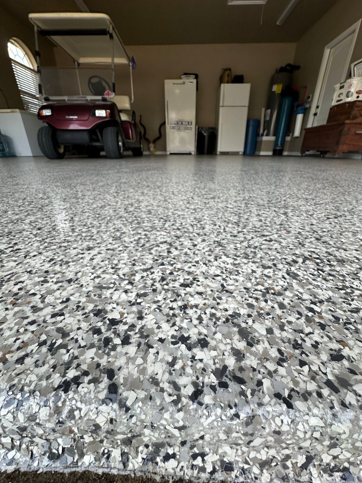 Garage with epoxy floor, burgundy golf cart, appliances, and storage. 