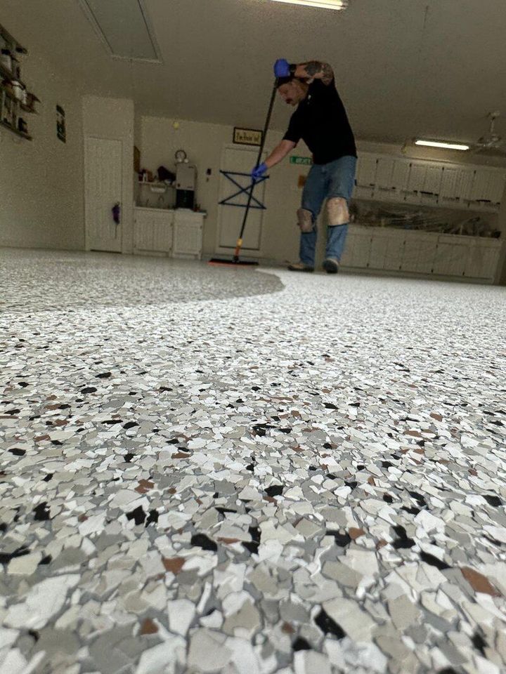 Man spreading polaspartic top coat in a garage. Flake epoxy flooring in foreground.