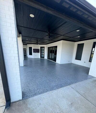 Covered outdoor patio with black ceiling and gray speckled floor. White brick columns and walls.