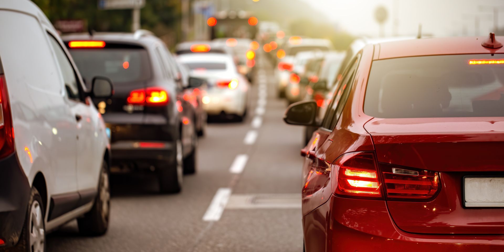 Traffic congestion on a multi-lane road featuring a prominent red sedan in the foreground and a line of various vehicles.