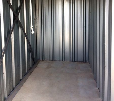 Empty storage unit with corrugated metal walls and a concrete floor.