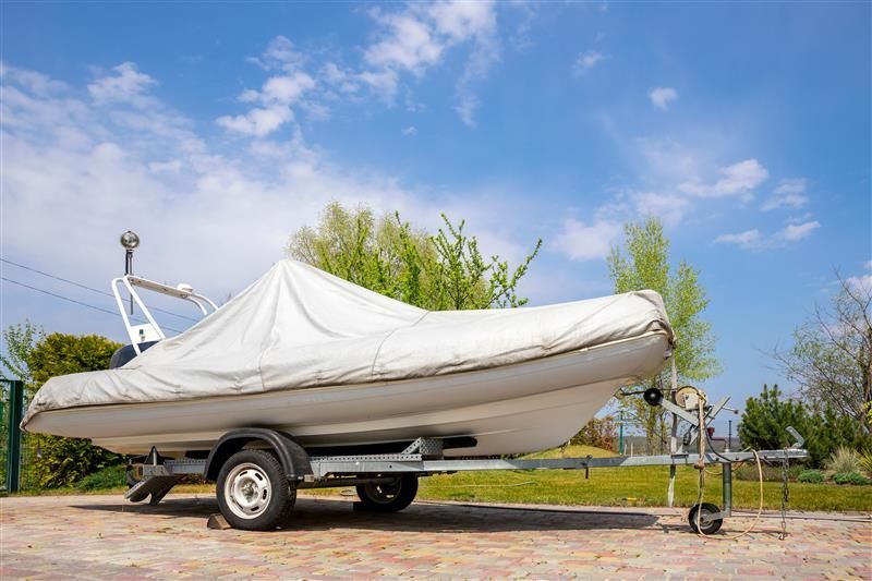 Boat on trailer covered with white tarp under blue sky.