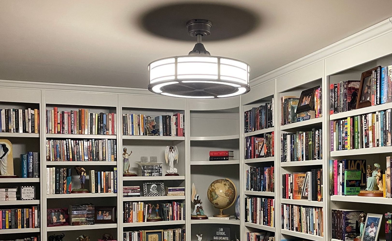 A library filled with books and a fan hanging from the ceiling.