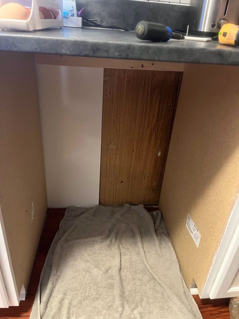 A kitchen cabinet with a towel on the floor underneath it.