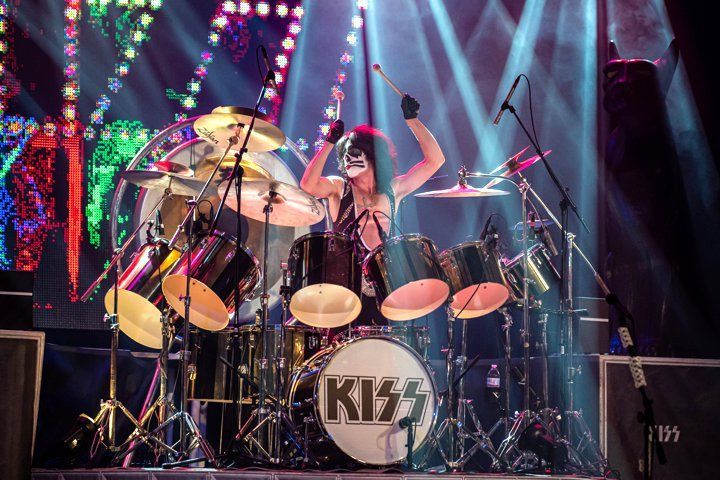 a man in a kiss mask is playing drums on a stage .