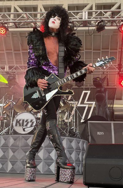 a man is playing a guitar on stage with a kiss logo in the background