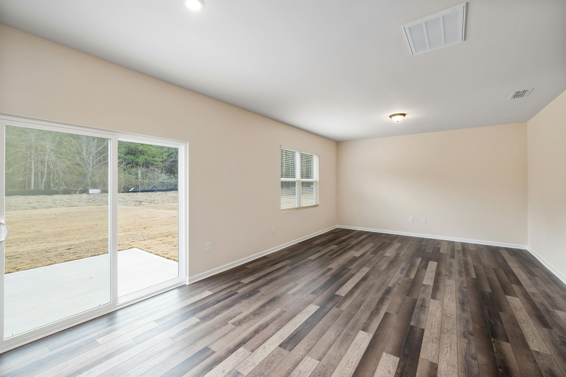 Empty room with wood-look floor, sliding glass door to patio, and small window. Beige walls and white trim.