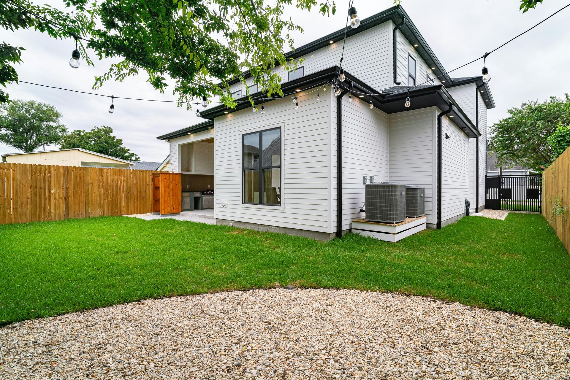 Backyard with white house, green grass, gravel patio, and wooden fence.