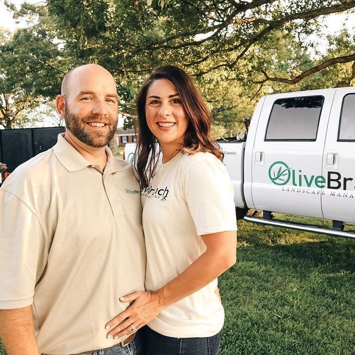 A man and a woman are posing for a picture in front of an olive branch truck